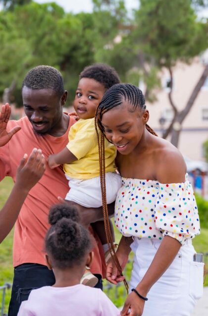 African black ethnicity family having fun with happy children together in city park, giving each other a hug